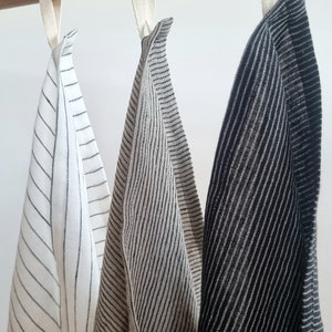 May include: Three striped kitchen towels hanging on a wooden rod. The towels are white with black stripes, beige with black stripes, and black with white stripes.
