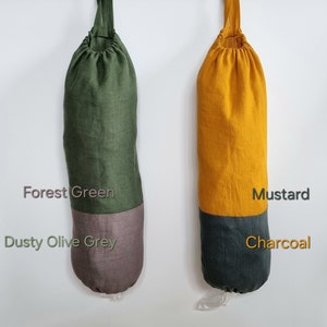 May include: Two reusable grocery bag holders. The one on the left is forest green with a dusty olive grey bottom. The one on the right is mustard yellow with a charcoal grey bottom. Both have a drawstring top and a plastic liner.