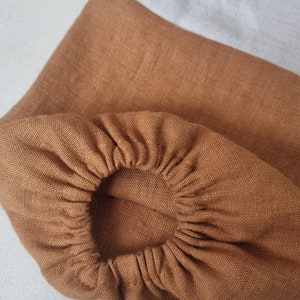 May include: A brown linen fabric with a gathered elastic band. The fabric is a light brown color and has a soft, textured feel.