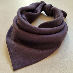 May include: A dark purple bandana made of a soft, textured fabric. The bandana is folded and tied in a knot at the top.