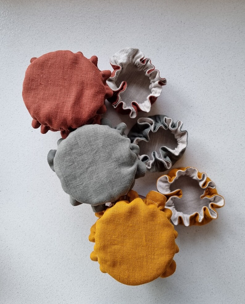 May include: Five fabric food covers in various colors and sizes. The covers are made of a natural linen material and have a ruffled edge. The colors are rust, gray, yellow, and white.