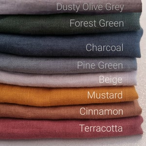 May include: A stack of fabric swatches in various colors, including dusty olive grey, forest green, charcoal, pine green, beige, mustard, cinnamon, and terracotta. The fabric swatches are arranged from lightest to darkest.