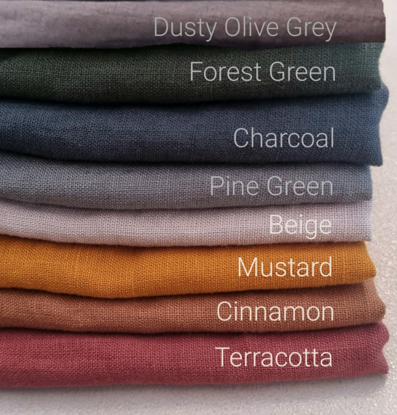 May include: A stack of fabric swatches in various colors, including dusty olive grey, forest green, charcoal, pine green, beige, mustard, cinnamon, and terracotta. The fabric swatches are arranged from lightest to darkest.