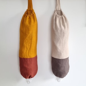 Könnte beinhalten: Zwei wiederverwendbare Einkaufstaschen hängen an einer Holzstange. Die Tasche links ist senfgelb mit einem burgunderfarbenen Boden. Die Tasche rechts ist beige mit einem dunkelgrauen Boden.