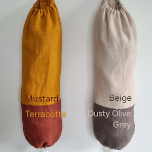 May include: Two reusable grocery bags made of linen fabric. The bag on the left is mustard yellow with a terracotta bottom. The bag on the right is beige with a dusty olive and grey bottom. Both bags have a drawstring closure and a loop for hanging.