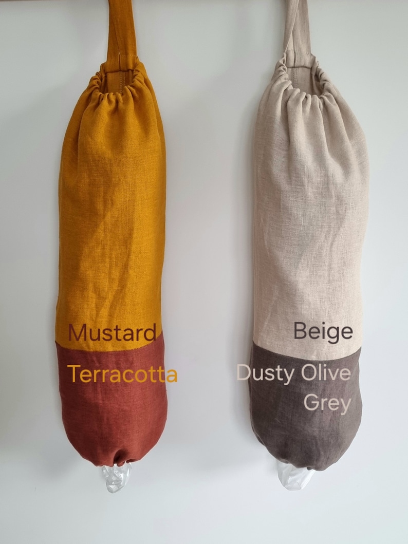 May include: Two reusable grocery bags made of linen fabric. The bag on the left is mustard yellow with a terracotta bottom. The bag on the right is beige with a dusty olive and grey bottom. Both bags have a drawstring closure and a loop for hanging.