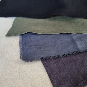 May include: Four fabric squares in different shades of blue, green, and black. The squares are arranged in a stack, with the black square on top and the blue square on the bottom. The fabric has a slightly textured surface.