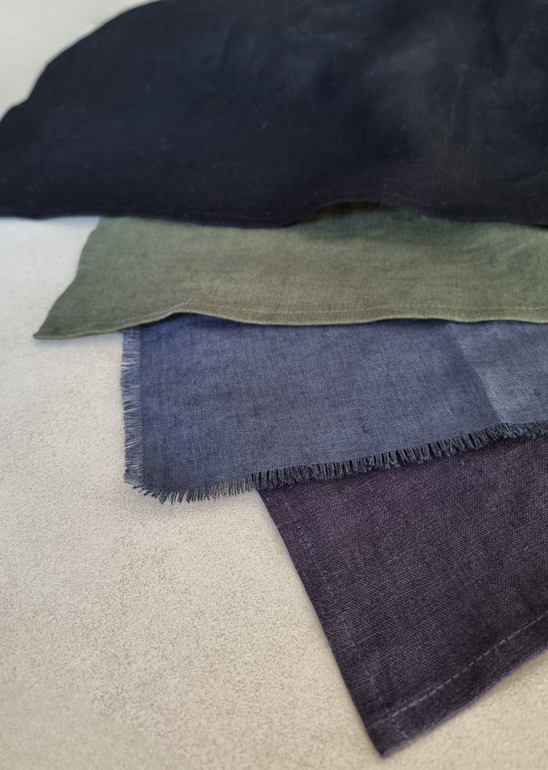 May include: Four fabric squares in different shades of blue, green, and black. The squares are arranged in a stack, with the black square on top and the blue square on the bottom. The fabric has a slightly textured surface.
