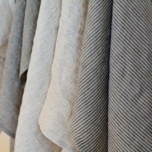 May include: Five kitchen towels hanging on a hook. The towels are made of linen and have a striped pattern. The towels are in shades of gray and white.