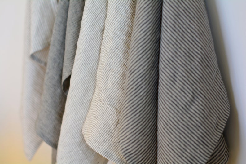 May include: Five kitchen towels hanging on a hook. The towels are made of linen and have a striped pattern. The towels are in shades of gray and white.