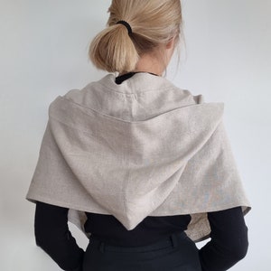 Peut inclure: Un châle à capuche en lin beige avec un design simple. Le châle est drapé sur les épaules d'une personne et la capuche est relevée.