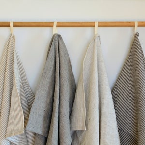 May include: Four striped linen kitchen towels hanging on a wooden rod. The towels are in various shades of brown and beige.