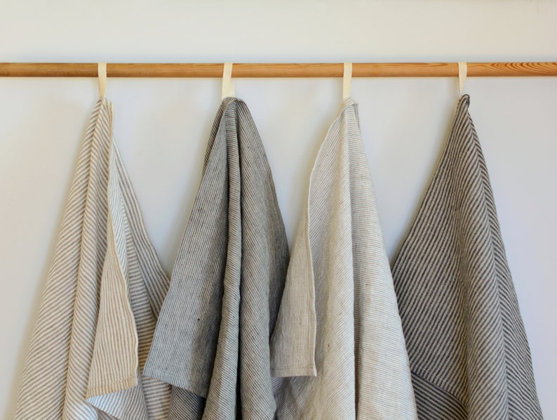 May include: Four striped linen kitchen towels hanging on a wooden rod. The towels are in various shades of brown and beige.