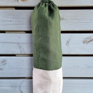 May include: A green and beige reusable grocery bag with a drawstring closure. The bag is hanging from a nail on a wooden wall.