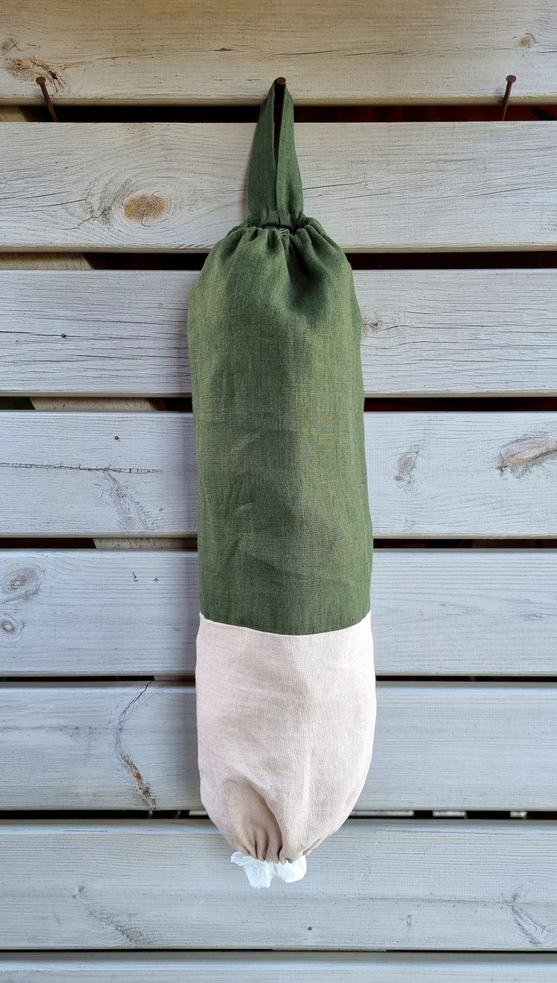 May include: A green and beige reusable grocery bag with a drawstring closure. The bag is hanging from a nail on a wooden wall.