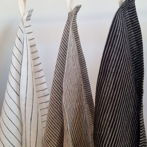 May include: Three striped kitchen towels hanging on a wooden rod. The towels are white with black stripes, beige with black stripes, and black with white stripes.