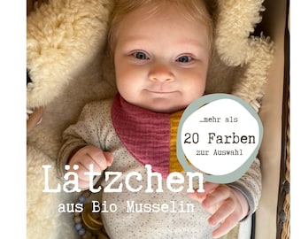 May include: A baby wearing a red and yellow bib with the text "...mehr als 20 Farben zur Auswahl" in a white circle. The baby is sitting in a white fluffy basket. The text "Lätzchen aus Bio Musselin" is below the baby.