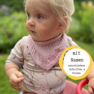 Könnte beinhalten: Ein Baby trägt einen rosa floralen Strampler und ein rosa Lätzchen mit dem Namen "Rosalie" bestickt. Das Lätzchen ist aus weichem, strukturiertem Stoff. Das Baby sitzt auf einem blauen und roten Spielzeug. Der Text "mit Namen" ist im Bild sichtbar, zusammen mit den Worten "verschiedene Schriften & Farben".