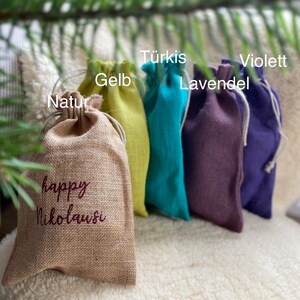 May include: Five small fabric gift bags in different colors. The bags are lined up from left to right: natural, yellow, turquoise, purple, and violet. The bag on the left has the text "happy Nikolaus" embroidered on it.