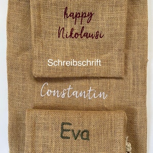 May include: Three burlap gift bags with different names embroidered on them. The top bag has the words "happy Nikolaus" in cursive, the middle bag has the name "Constantin" in cursive, and the bottom bag has the name "Eva" in block letters. The top bag also has the word "Schreibschrift" below the name, and the bottom bag has the word "Druckschrift" below the name.