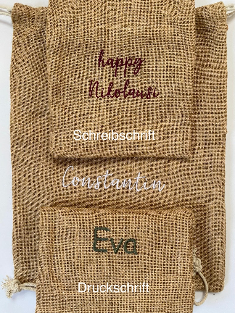May include: Three burlap gift bags with different names embroidered on them. The top bag has the words "happy Nikolaus" in cursive, the middle bag has the name "Constantin" in cursive, and the bottom bag has the name "Eva" in block letters. The top bag also has the word "Schreibschrift" below the name, and the bottom bag has the word "Druckschrift" below the name.