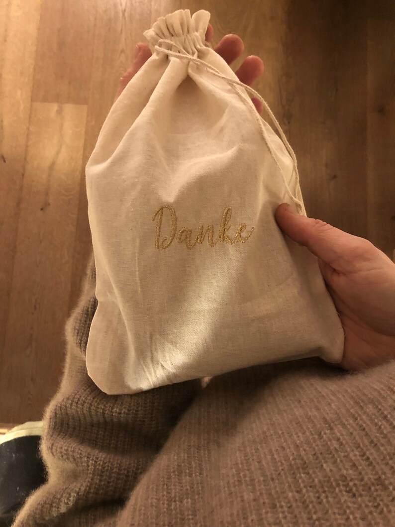May include: A white cotton drawstring bag with the word "Danke" embroidered in gold thread.