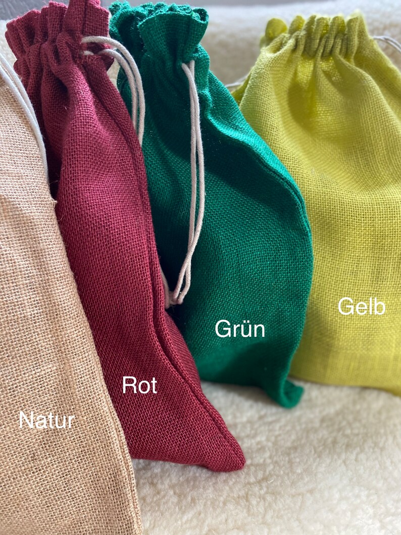 May include: Four drawstring bags made of natural fabric in different colors: natural, red, green, and yellow. The bags are labeled with the colors "Natur", "Rot", "Gr&uuml;n", and "Gelb".