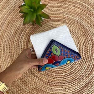 May include: A blue and white ceramic napkin holder with a floral design. The holder is shaped like a triangle and has a white napkin inside.