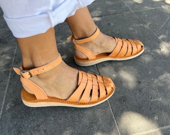 Può includere: Sandali in pelle color cuoio con cinturini intrecciati e una cinturino alla caviglia con chiusura a fibbia. I sandali hanno una suola piatta.