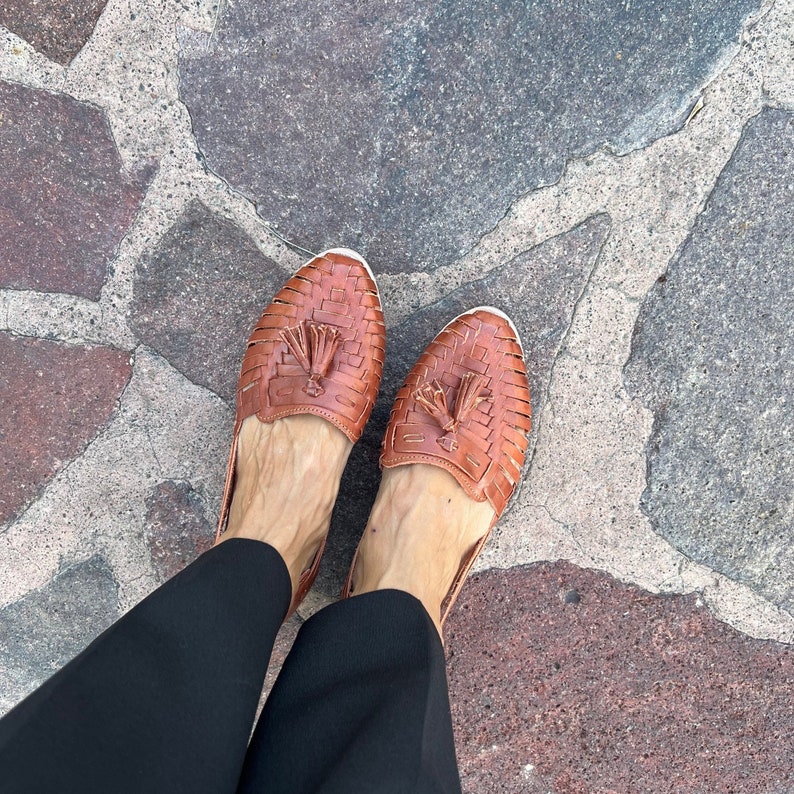 May include: A pair of brown leather sandals with tassels on a stone floor.