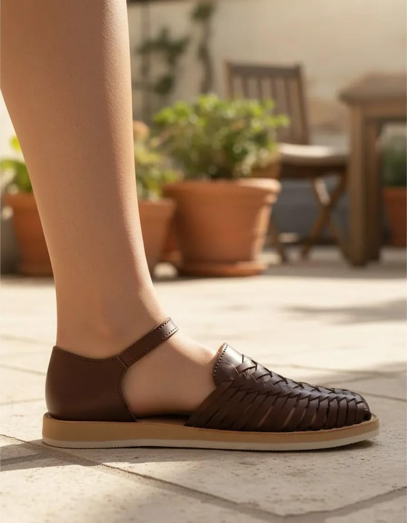 May include: Brown leather sandal with a woven design. The sandal features an ankle strap and a tan sole. The image shows the sandal on a person's foot.