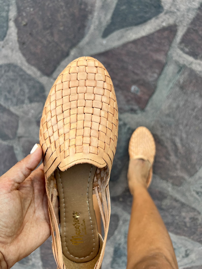 Puede incluir: Sandalias de cuero color canela con un dise&ntilde;o tejido. Las sandalias tienen una correa que va alrededor del tobillo y una peque&ntilde;a abertura en la punta. Las sandalias est&aacute;n hechas por la marca "Huichol" y tienen una suela de cuero.