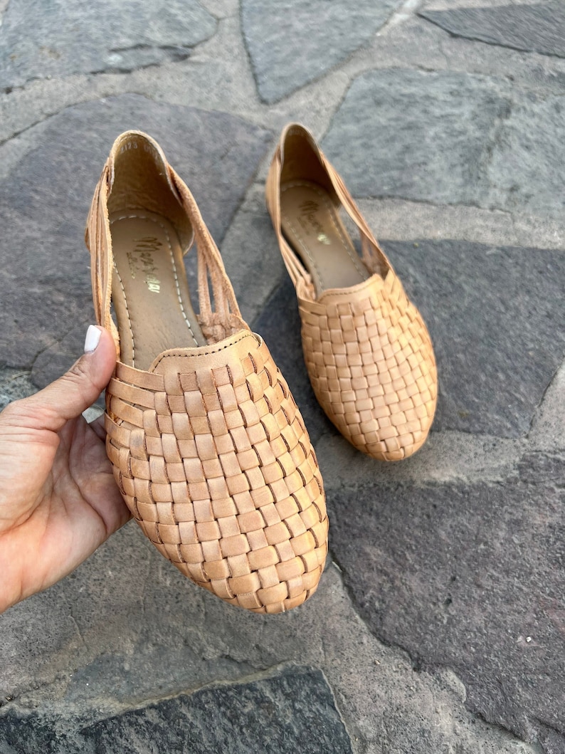 Puede incluir: Un par de sandalias de cuero trenzado de color marr&oacute;n claro. Las sandalias tienen un dise&ntilde;o sencillo con una parte superior trenzada y una suela plana.