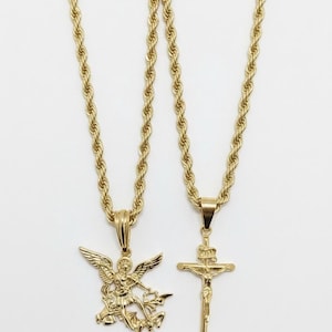 May include: Two gold-colored necklaces with pendants. One pendant depicts an angel with outstretched wings, and the other is a crucifix with a figure of Jesus. The chains have a rope-like design.