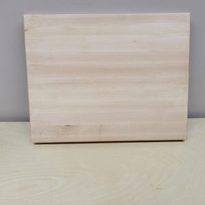 May include: A plain, light wood cutting board with a smooth surface.