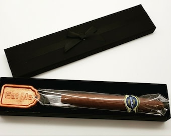 May include: A chocolate cigar presented in a black gift box with a ribbon. The cigar is wrapped in cellophane and has a "Sun Ray" label. A copper-coloured tag with "Eat Me" is also in the box.