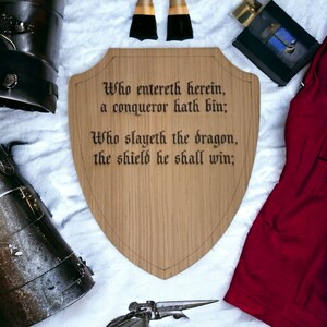 May include: A wooden shield with a medieval inscription: "Who entereth herein, a conqueror hath bin; Who slayeth the dragon, the shield he shall win;"