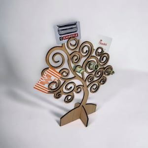 May include: A wooden tree-shaped gift card and money holder. The holder has a swirling branch design and holds gift cards from Chipotle, Chick-fil-A, and Whataburger, along with rolled-up dollar bills. The holder is made of light-colored wood.
