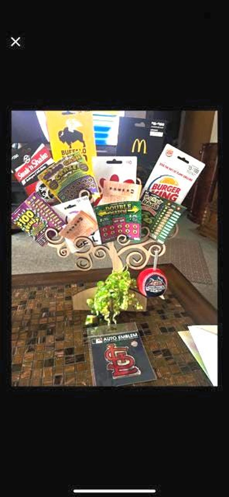 May include: A decorative arrangement featuring gift cards from various restaurants and businesses, including Burger King and McDonald's. The arrangement also includes lottery tickets and a St. Louis Cardinals auto emblem.