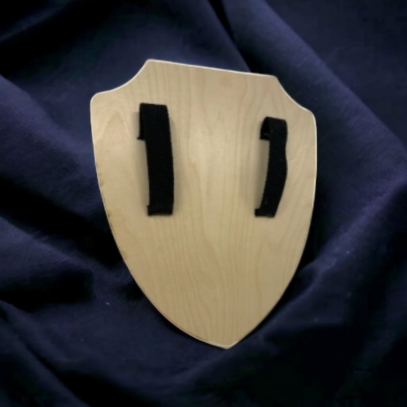 May include: A wooden shield with a light brown finish and two black straps on the back.