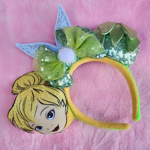 May include: Tinkerbell themed Minnie Mouse ears headband with a green bow, a green flower, and a Tinkerbell face on one ear.