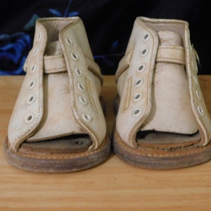 May include: A pair of white leather orthopedic sandals with adjustable straps and multiple eyelets. The sandals have a brown rubber sole.