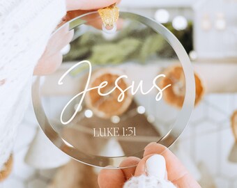 May include: Clear round glass ornament with the word "Jesus" and the Bible verse "Luke 1:31" written in white.