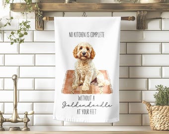 May include: White kitchen towel featuring a watercolor illustration of a Goldendoodle dog sitting on a rug. The towel has the text "NO KITCHEN IS COMPLETE WITHOUT A Goldendoodle AT YOUR FEET" in black script.