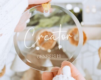 May include: A clear glass ornament with the word "Creator" and the text "Genesis 1:1" in white lettering.