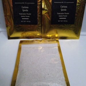 May include: Two gold foil pouches with black labels that read "Ms. G's Curious Goods Destruction Powder Satchel Powder NET WT. 1 OZ (28g)". A third pouch is open and shows a white powder inside.