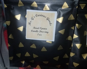 Könnte beinhalten: Ein schwarzer Beutel mit goldenen Dreiecksmuster und einem weißen Etikett mit der Aufschrift "Ms. G's Curious Goods Road Opener Candle Dressing 1 oz."
