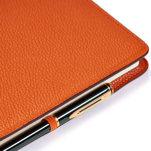 May include: A close-up of an orange leather-bound notebook with a gold pen tucked into the cover.