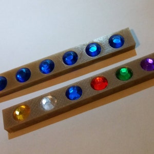 May include: Two beige strips with rows of colorful rhinestones. The top strip has blue rhinestones, the bottom strip has gold, silver, blue, red, green, and purple rhinestones.