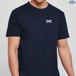 Op de afbeelding: Marineblauw T-shirt met een klein embleem van een wit en blauw vlag op de borst. Het shirt met korte mouwen heeft een ronde hals en is gemaakt van een zacht materiaal. Het embleem is een witte X op een blauwe achtergrond.